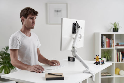 Back view of user working at desk with Flo single monitor arm, desk-clamp mounted with adjustable angle and length joints