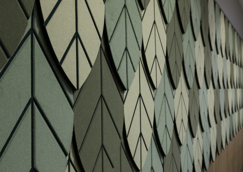 A wall covered in Autex Vertiface acoustic panels arranged in a geometric pattern, featuring various shades of green and gray.
